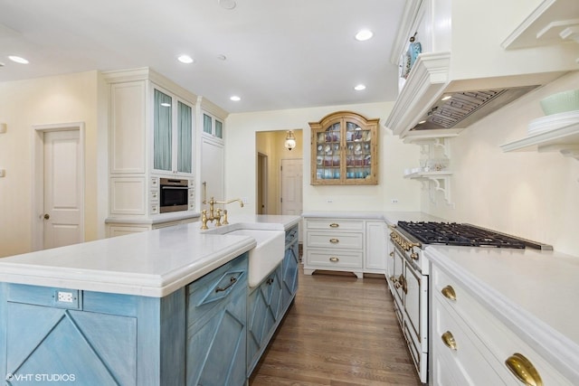 kitchen featuring dark hardwood / wood-style floors, gas stove, a center island with sink, white cabinetry, and custom range hood