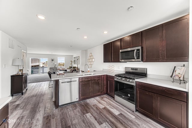 kitchen featuring sink, stainless steel appliances, kitchen peninsula, wood-type flooring, and a breakfast bar