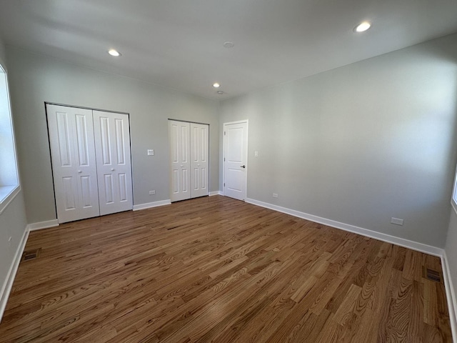 unfurnished bedroom featuring hardwood / wood-style floors and two closets