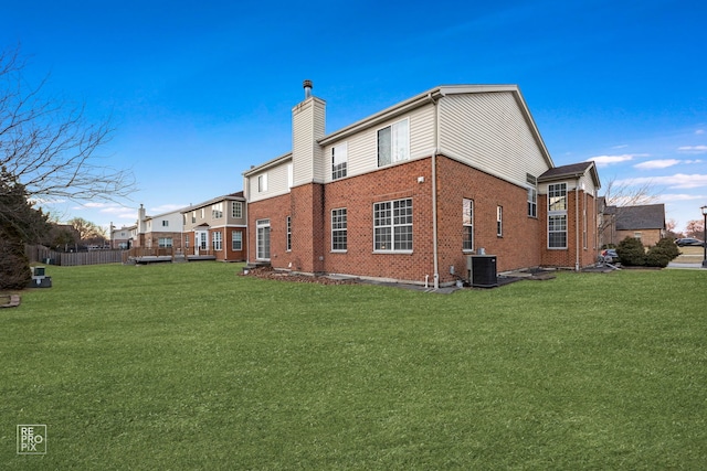 back of property with a chimney, a lawn, central AC, and brick siding