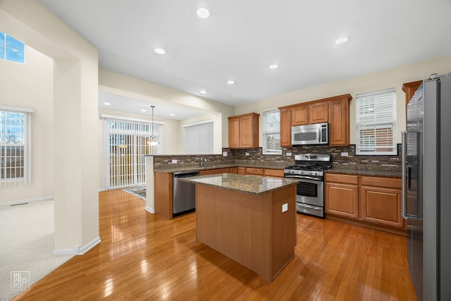 kitchen with a peninsula, a sink, appliances with stainless steel finishes, decorative backsplash, and a center island