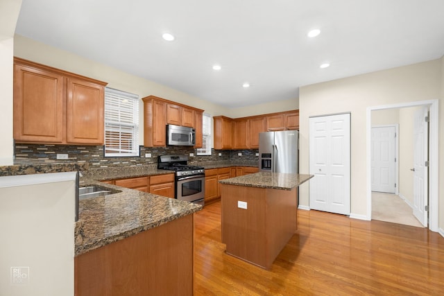 kitchen featuring light wood-style flooring, stainless steel appliances, a kitchen island, backsplash, and dark stone countertops