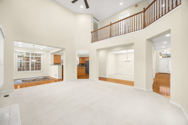 unfurnished living room featuring recessed lighting, ceiling fan with notable chandelier, light colored carpet, visible vents, and baseboards