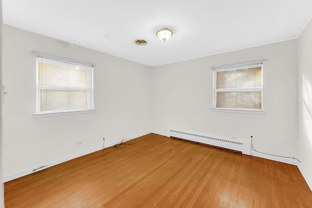 empty room with wood-type flooring, a baseboard radiator, and a wealth of natural light