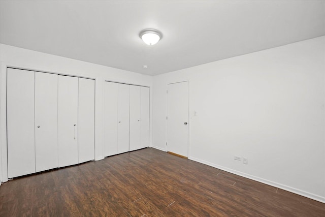 unfurnished bedroom featuring dark hardwood / wood-style floors and multiple closets