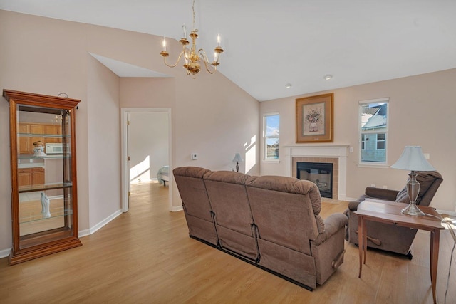 living room featuring light wood-type flooring, lofted ceiling, a fireplace, and a chandelier