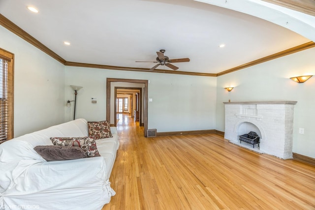 living room with ceiling fan, light hardwood / wood-style flooring, crown molding, and a fireplace