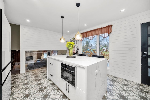 kitchen with pendant lighting, a center island, oven, wooden walls, and light stone countertops