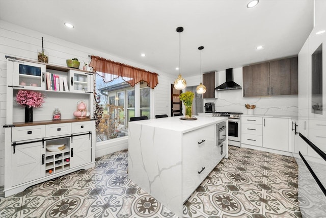 kitchen with light stone countertops, a center island, stainless steel stove, wall chimney range hood, and white cabinets