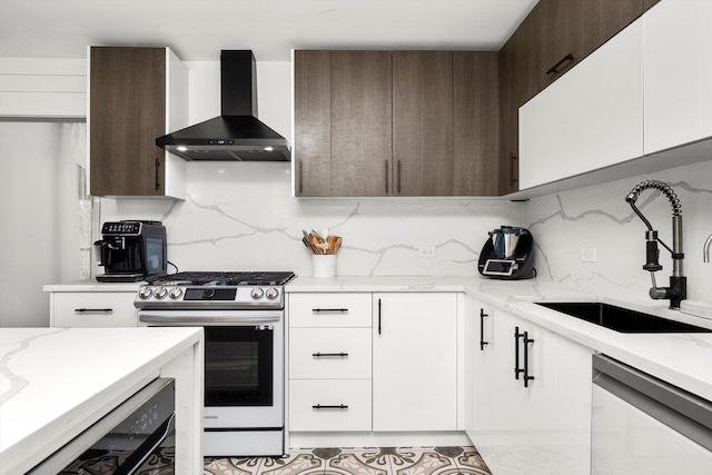 kitchen featuring wall chimney exhaust hood, dishwashing machine, sink, stainless steel range oven, and white cabinets