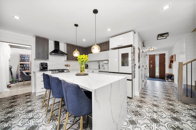 kitchen with white cabinetry, a center island, wall chimney exhaust hood, decorative light fixtures, and decorative backsplash