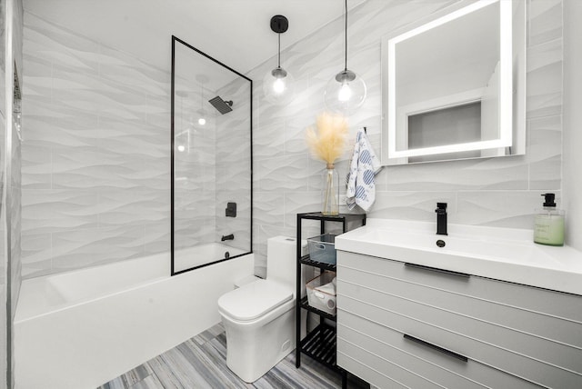 full bathroom featuring vanity, toilet, tiled shower / bath, and tile walls