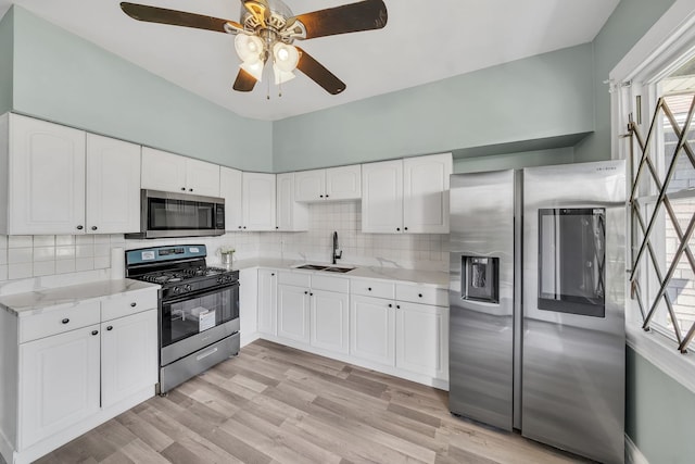 kitchen with white cabinets, sink, appliances with stainless steel finishes, and light hardwood / wood-style flooring