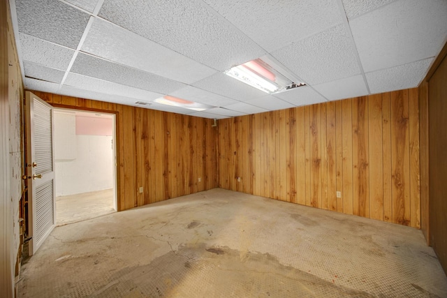 basement featuring wood walls and a drop ceiling