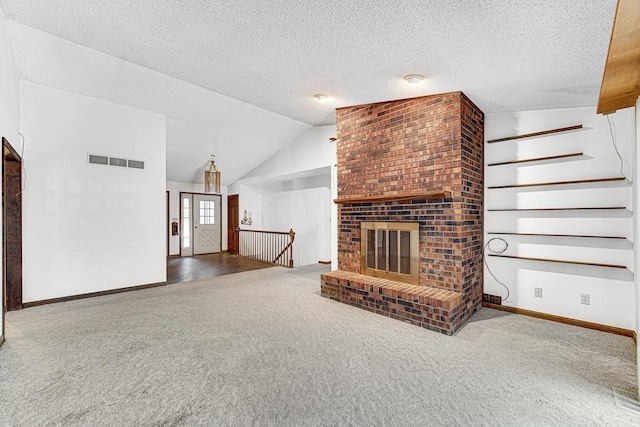 unfurnished living room with lofted ceiling, a brick fireplace, a textured ceiling, and carpet flooring