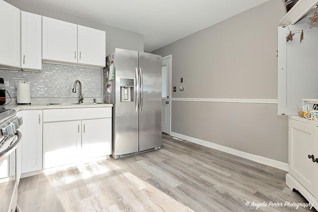 kitchen with appliances with stainless steel finishes, backsplash, light wood-type flooring, sink, and white cabinets