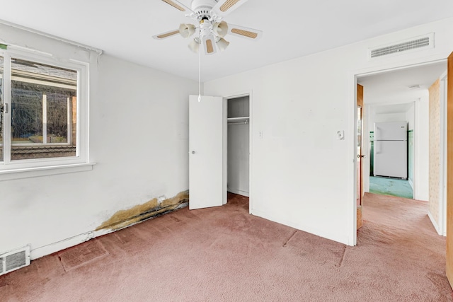 unfurnished bedroom with light carpet, white refrigerator, a closet, and ceiling fan