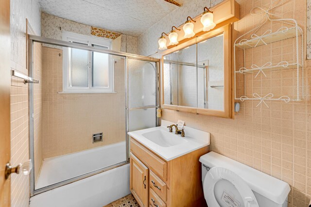 full bathroom featuring toilet, combined bath / shower with glass door, tile walls, and vanity