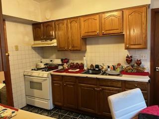 kitchen featuring ventilation hood, backsplash, white stove, and dark tile patterned flooring