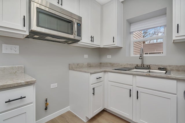 kitchen featuring white cabinetry, sink, light stone counters, and light wood-type flooring