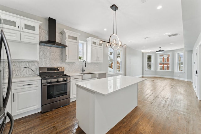 kitchen featuring dark wood-type flooring, a sink, stainless steel appliances, wall chimney exhaust hood, and light countertops