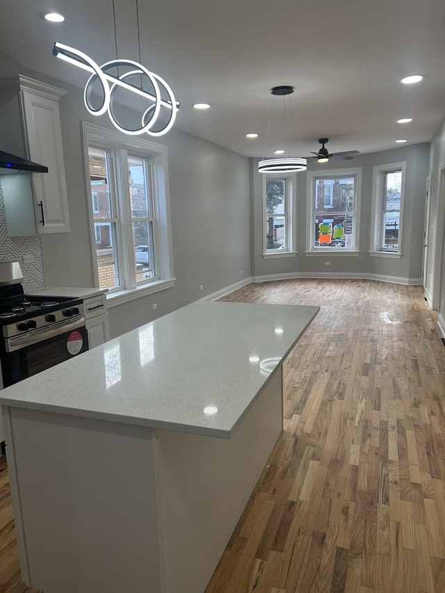 kitchen featuring light wood-type flooring, white cabinetry, stainless steel range with gas cooktop, wall chimney range hood, and ceiling fan