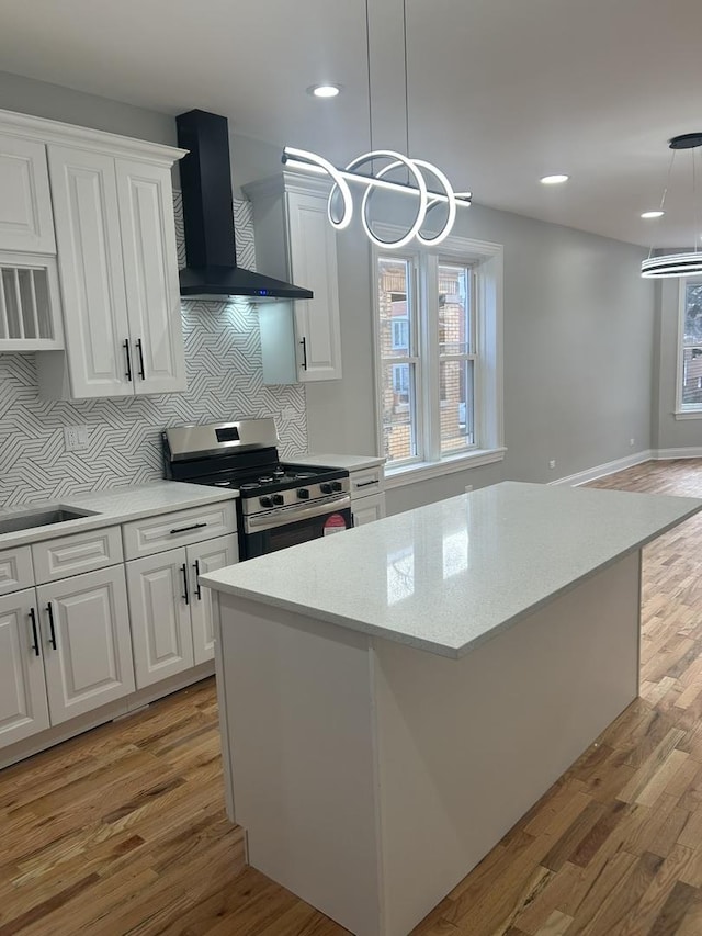 kitchen with stainless steel gas range, an inviting chandelier, light wood-style flooring, white cabinets, and wall chimney exhaust hood