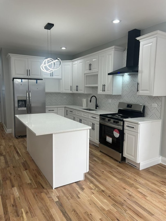 kitchen featuring light wood-style flooring, a sink, light countertops, appliances with stainless steel finishes, and wall chimney range hood