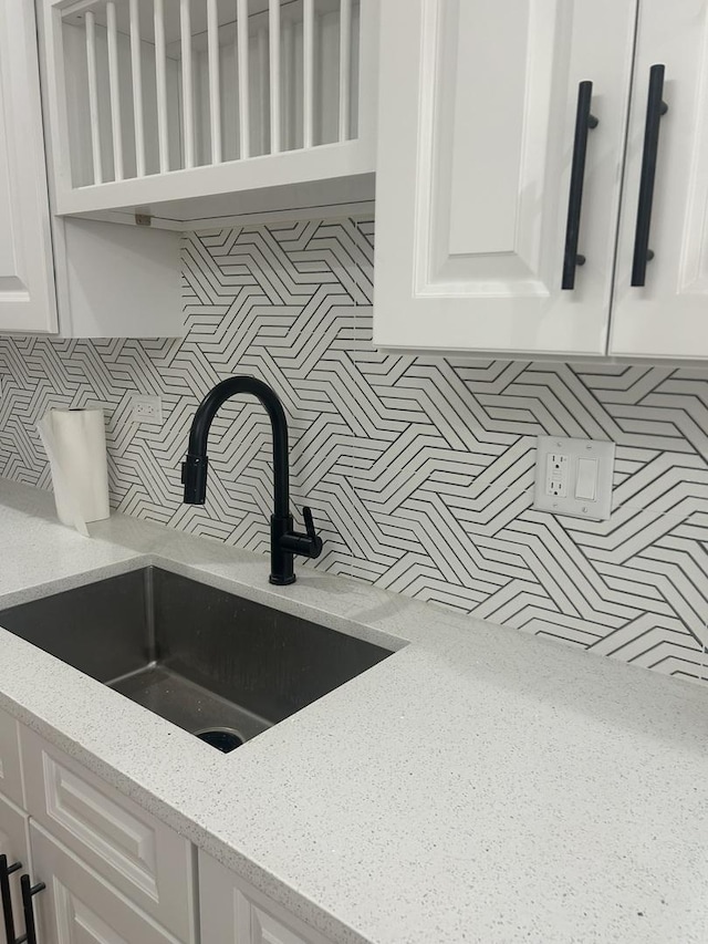 interior details featuring light stone counters, decorative backsplash, white cabinetry, and a sink