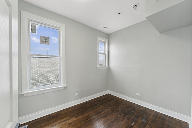 unfurnished room featuring dark wood-style flooring, visible vents, baseboards, and a wealth of natural light