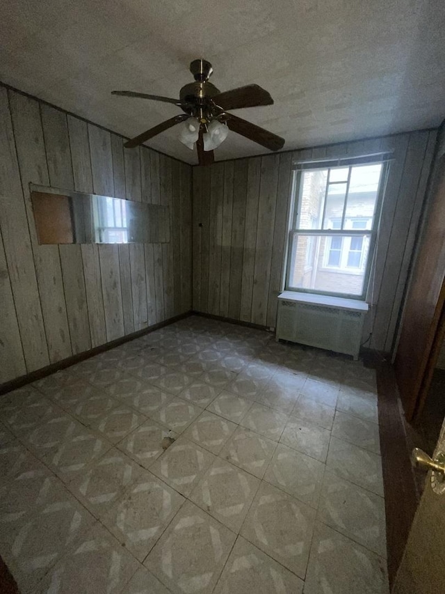 unfurnished room with wood walls, radiator heating unit, and ceiling fan