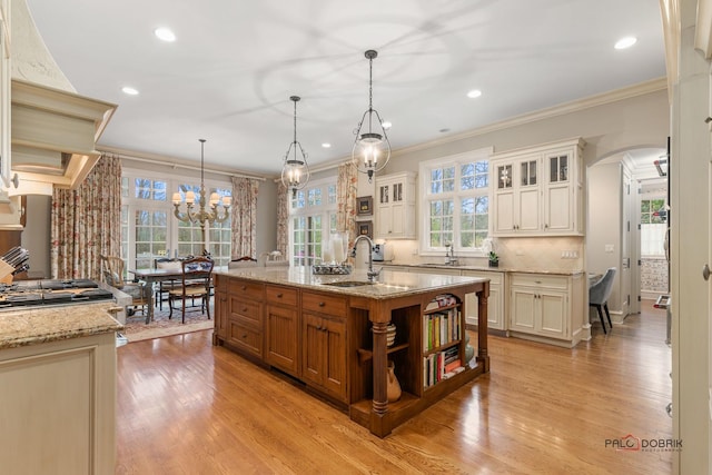 kitchen featuring sink, a center island with sink, ornamental molding, and hanging light fixtures