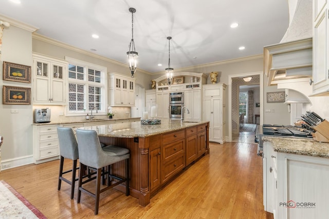 kitchen featuring a large island with sink, decorative light fixtures, light hardwood / wood-style flooring, and light stone counters