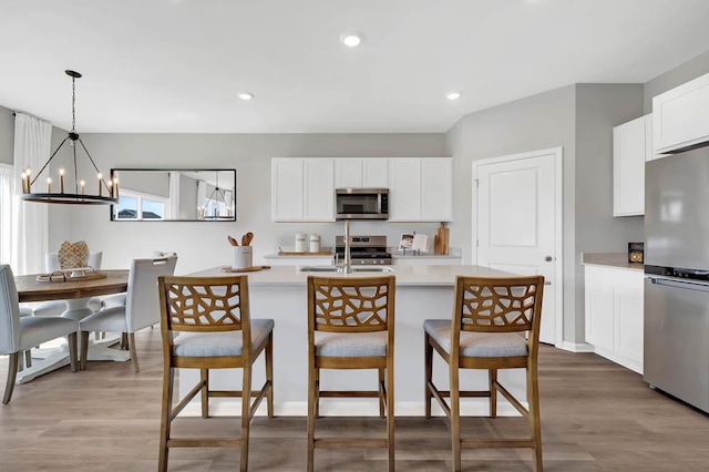 kitchen with appliances with stainless steel finishes, decorative light fixtures, an inviting chandelier, light hardwood / wood-style flooring, and white cabinets