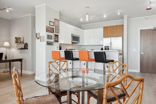 dining area featuring light wood-style floors, track lighting, crown molding, and baseboards