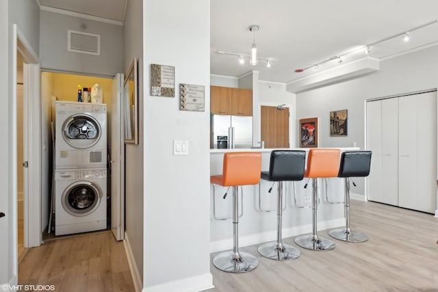 kitchen featuring visible vents, stainless steel fridge, a kitchen bar, stacked washer and clothes dryer, and crown molding