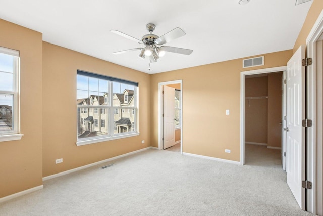 unfurnished bedroom featuring a walk in closet, ceiling fan, a closet, and light carpet