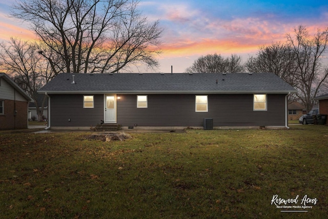 back house at dusk with a lawn and central air condition unit