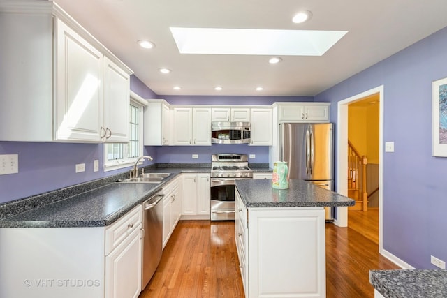 kitchen with a skylight, stainless steel appliances, sink, white cabinetry, and a kitchen island