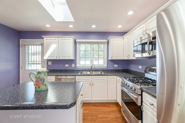 kitchen featuring a center island, white cabinets, sink, a skylight, and appliances with stainless steel finishes