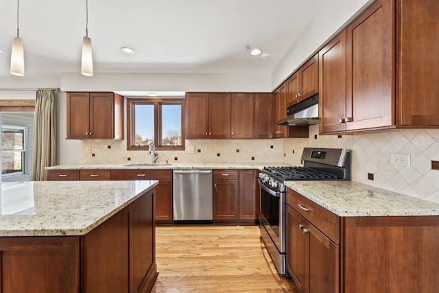 kitchen with sink, hanging light fixtures, stainless steel appliances, light stone countertops, and light wood-type flooring