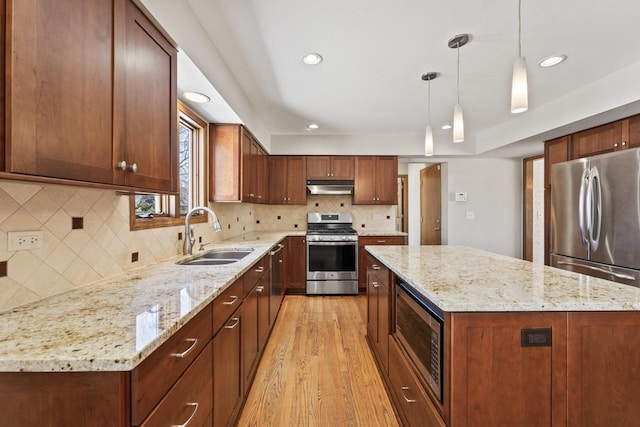 kitchen featuring sink, appliances with stainless steel finishes, a kitchen island, pendant lighting, and light stone countertops