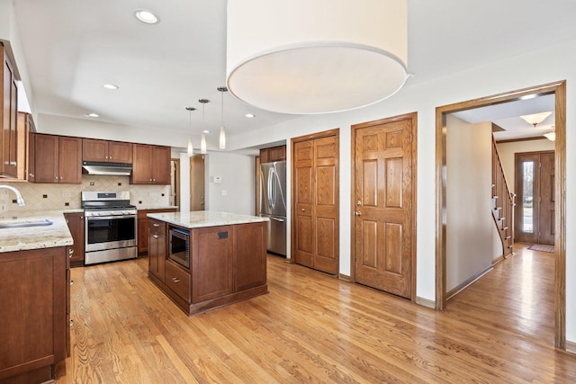 kitchen with sink, appliances with stainless steel finishes, a center island, light stone counters, and decorative light fixtures