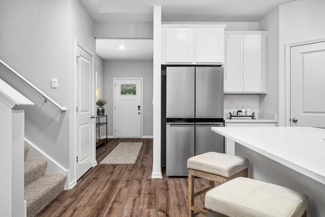 kitchen featuring white cabinets, dark hardwood / wood-style floors, stainless steel fridge, and a kitchen bar