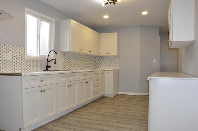 kitchen with sink, white cabinets, decorative backsplash, and light hardwood / wood-style flooring