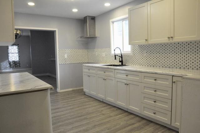 kitchen featuring sink, white cabinets, and wall chimney range hood