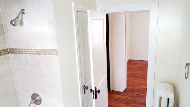 bathroom featuring hardwood / wood-style floors, tiled shower, and radiator