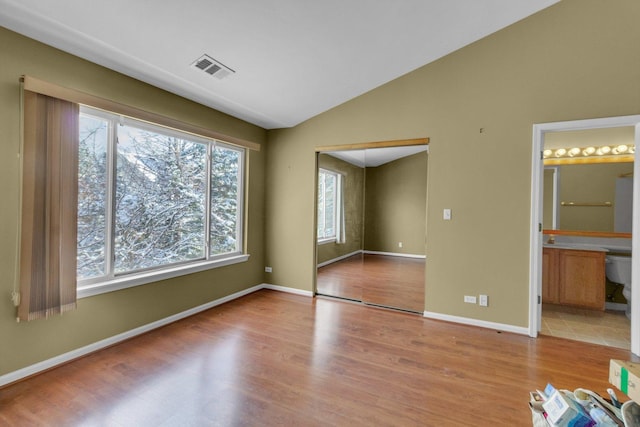 unfurnished bedroom with connected bathroom, a closet, lofted ceiling, and light hardwood / wood-style flooring