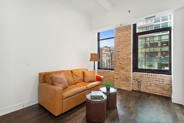 living room featuring beamed ceiling, dark wood-type flooring, and brick wall