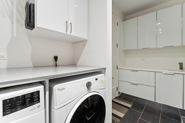 clothes washing area featuring cabinets, sink, dark tile patterned flooring, and washing machine and clothes dryer